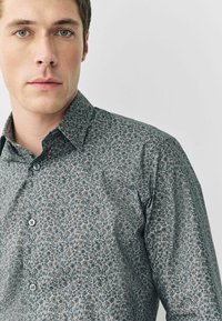 Graues Langarmhemd mit floralem Muster in Grün und Beige, mit Button-Down-Kragen und zwei vorderen Knöpfen.