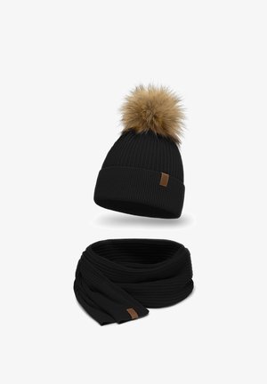 Berretto di lana nera con pon-pon in pelliccia marrone sulla parte superiore e sciarpa nera a coste coordinata, entrambi con una piccola etichetta in pelle marrone.