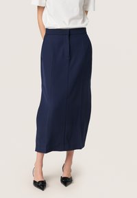 Marineblaue, knielange Rock mit taillierter Passform, Seitentaschen und glatter Textur; kombiniert mit spitzen schwarzen High Heels.