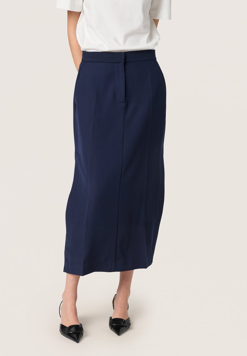 Marineblaue, knielange Rock mit taillierter Passform, Seitentaschen und glatter Textur; kombiniert mit spitzen schwarzen High Heels.