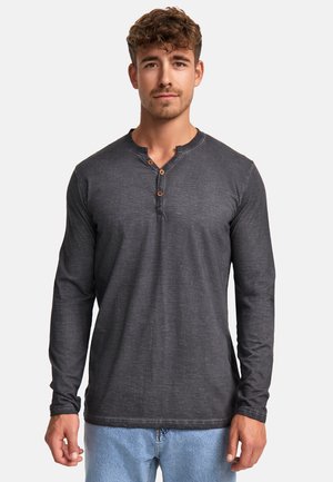 Camisa Henley de manga larga en gris oscuro con un acabado texturizado y tres botones de madera en la tapeta, combinada con jeans de color azul claro.