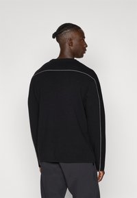 Maglione nero a maglia con maniche lunghe, collo rotondo e dettagli bianchi sottili lungo la cucitura posteriore. Texture morbida e vestibilità rilassata.