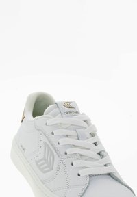 Białe sneakersy z teksturowanej skórzanej cholewki, z zapięciem na sznurówki i jasnoszarymi akcentami. Posiadają logo marki oraz brązowy uchwyt na pięcie.