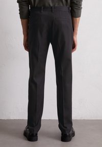 Pantaloni neri con vestibilità su misura, caratterizzati da una texture liscia, passanti per cintura e due tasche posteriori. Indossati con scarpe nere.