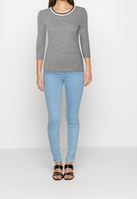 Randig långärmad topp i grått och vitt, med rund halsringning och trekvartsärmar, tillsammans med ljusblå skinny jeans och svarta sandaler.