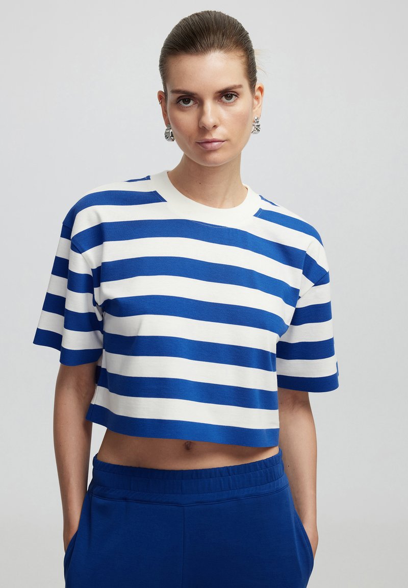 Camiseta recortada de rayas azules y blancas, hecha de tejido suave, con cuello redondo y mangas cortas, combinada con pantalones elásticos azules.