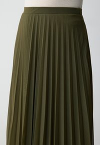 Gonna midi plissettata in verde oliva, realizzata in tessuto leggero. Presenta una cintura in vita e un design fluido e testurizzato con pieghe verticali.