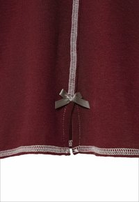 Maroon tkanina s teksturiranom završnom obradom. Značajni detalji uključuju bijelu šavnu obrub i mali sivi mašnu kao akcent.