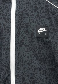 Črno-siva tkanina s črnim in sivim vzorcem, belo zadrgo in črno Nike Air logo značko na desni strani.