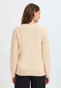 Beige svetr s dlouhými rukávy, kulatým výstřihem a žebrovanými manžetami. Měkká textura a minimalistický design, přiléhavý v pase.