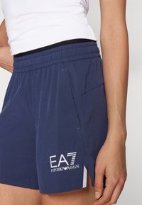 Calções de atletismo azul-marinho com um cós elástico, bolso lateral, detalhes em logo branco e acentos em malha para respirabilidade.
