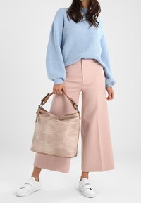 Maglione azzurro a coste, pantaloni rosa a gamba larga e una borsa beige testurizzata con parte superiore arrotondata e manici marroni. Sneakers bianche senza lacci.