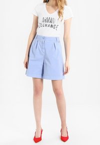 Světle modré bavlněné šortky s plisováním, zapínáním na knoflík a bočními kapsami. Doplňují je bílé tričko s černým textem. Červené vysoké podpatky.