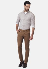 Koszula zapinana z małymi ciemnymi wzorami na białym tle, w połączeniu z dopasowanymi brązowymi spodniami i ciemnymi skórzanymi butami.