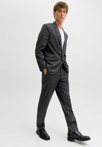 Męski ciemnoszary garnitur w cienkie prążki wykonany z gładkiej tkaniny; krój slim-fit z klapą z wycięciem, kieszeniami, zestawiony z czarnymi wizytowymi butami.