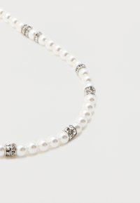 Λευκό κολιέ από πέρλες με ασημένιους διαχωριστές με στρας σε απλό ανοιχτό φόντο.