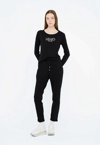 Schwarzes Langarmshirt mit dem Aufdruck "LIU JO MILANO" in Weiß, kombiniert mit schwarzen Jogginghosen mit Kordelzug und goldfarbenen Hardware-Akzenten.