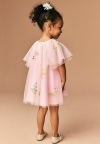 Rosa Tüllkleid mit floralem Stickerei, kurzen Rüschensäumen und einem weit schwingenden Rock. Silberne Schuhe mit runder Zehenpartie und Schnallendetails.