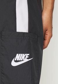 Black Nike shorts featuring a white logo, side pocket, and contrasting white vertical stripe on the outer seam.  Made from lightweight material.