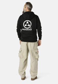 Zwarte hoodie met witte "MOLECULE" logo, gecombineerd met licht beige cargobroek met meerdere zakken en een relaxte pasvorm.