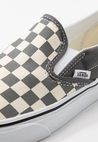 Chaussure Vans slip-on avec motif damier noir et blanc et semelle en caoutchouc blanche vue de côté et de dessus.