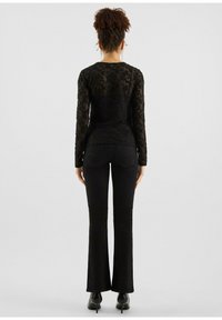 Schwarzes Spitzenoberteil mit langen Ärmeln und floralen Mustern, kombiniert mit schwarzen ausgestellten Jeans. Das Outfit wird mit schwarzen Absatzstiefeln abgerundet.
