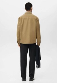 Brown wool blend jacket with a collar, buttoned cuffs, and a straight cut. Paired with black trousers, holding a dark scarf.
