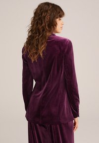Fialový sametový blazer s dlouhými rukávy a přiléhavým střihem. Obsahuje knoflíkové detaily na manžetách a hladkou texturu. Zobrazeno ze zadní strany.