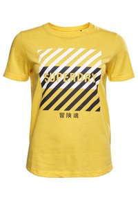Camiseta de algodón amarilla con un gráfico audaz que presenta rayas diagonales en blanco y negro, y la palabra "SUPERDRY" en un tipo de letra grande.
