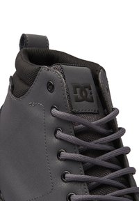 Ciemnoszare, wysokie buty sportowe z syntetycznej skóry, czarnym materiałowym kołnierzem, szarymi sznurowadłami oraz metką z logo.