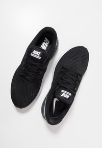 Scarpe da corsa Nike nere con tomaia in rete, superficie testurizzata, lacci e accento di swoosh Nike bianco. Presentano ammortizzazione e colletto imbottito.