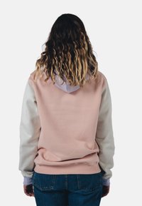 Mikina s kapucí, která má růžovou zadní část a bílé rukávy, strukturovanou tkaninu, žebrované manžety a světle fialovou vnitřní kapuci.