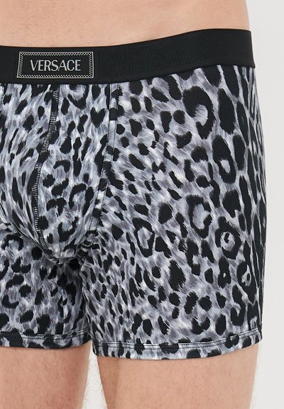 Mann iført Versace boxershorts med svart og grå leopardmønster og svart midjebånd med Versace-logo.