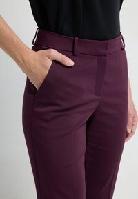Pantalons ajustés bordeaux avec une texture lisse, dotés d'une poche latérale et de passants de ceinture, stylisés avec une taille cintrée.