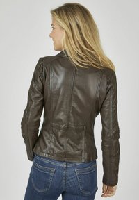 Braune Lederjacke mit einem taillierten Design, gepolsterten Schultern und sichtbaren Nähdetails. Kombiniert mit blauen Jeans.