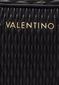 Juodas kvadratuotas odinis rankinukas, puikuojantis auksiniu "Valentino" logotipu, su tekstūruotu paviršiumi ir deimantų formos raštu.