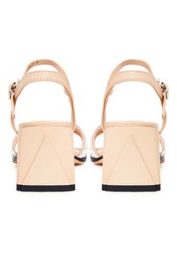 Beige Riemchensandalen mit blockförmigen Absätzen, mit schwarzem Untergrund und silbernen Verzierungen an den Riemen. Glatte Ledertextur.