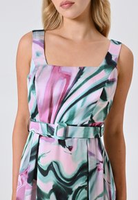 Ärmelloses Kleid aus weichem Stoff mit einem quadratischen Ausschnitt. Wirbelnde Muster in Pink, Grün und Weiß, mit einem passenden Gürtel und quadrischer Schnalle.