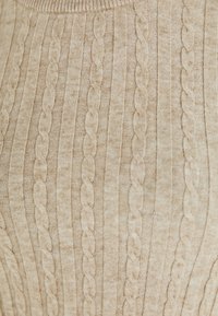 Tessuto a maglia beige con motivi a treccia verticale e a coste, che mostrano la texture e le fibre morbide in primo piano.