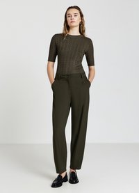 Top a maglia verde oliva con maniche corte, caratterizzato da un motivo a trecce. Pantaloni verdi oliva larghi con tasche laterali e bottone. Mocassini neri.