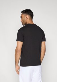 Czarny bawełniany t-shirt z krótkimi rękawami, okrągłym dekoltem i gładką teksturą. Widok od tyłu, prezentowany na neutralnym tle.