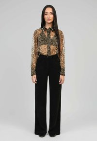 Blouse transparente avec imprimé animal en marron et noir, associée à un pantalon large taille haute noir. Des chaussures noires simples viennent compléter le look.