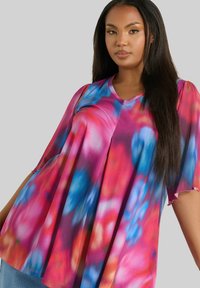 Blusa colorata e multicolore con scollo a V, vestibilità ampia e maniche corte. Il tessuto ha una consistenza liscia con un motivo tie-dye di rosa e blu.