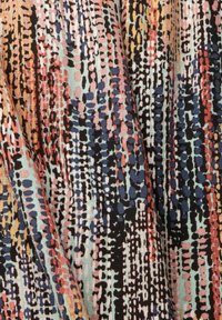 Tissu multicolore avec des motifs abstraits en points et en tirets noirs, bleus, rouges, orange et beige, montrant des plis drapés et une texture.