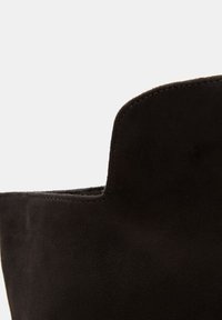 Botín de ante negro, con un borde superior curvado, textura suave y sutilezas en las costuras. El diseño es mínimo y contemporáneo.