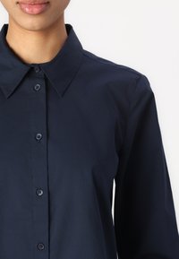 Navy blue button-up shirt with a pointed collar, long sleeves, and seven front buttons. The fabric appears smooth and lightweight.