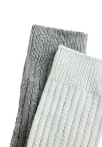 Due calzini in lana a coste, uno grigio chiaro e uno grigio scuro, sovrapposti su uno sfondo bianco.