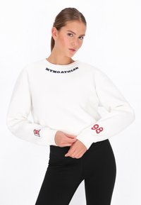 Sudadera blanca con el texto "MYMOATHLSR" en el cuello, número "98" en rayas rojas en la manga, y pantalones leggings negros. Tejido liso, cuello redondo.