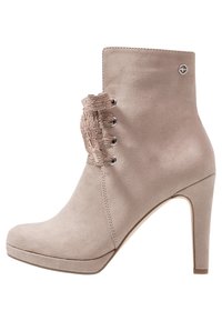 Beige suede high-heeled ankle boot with lace-up front featuring decorative lace, rounded toe, and small metallic circular logo near the top.