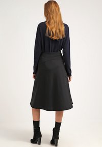 Falda negra, hasta la rodilla, con una textura suave y un diseño envolvente, combinada con un suéter oscuro y botas negras de tacón.